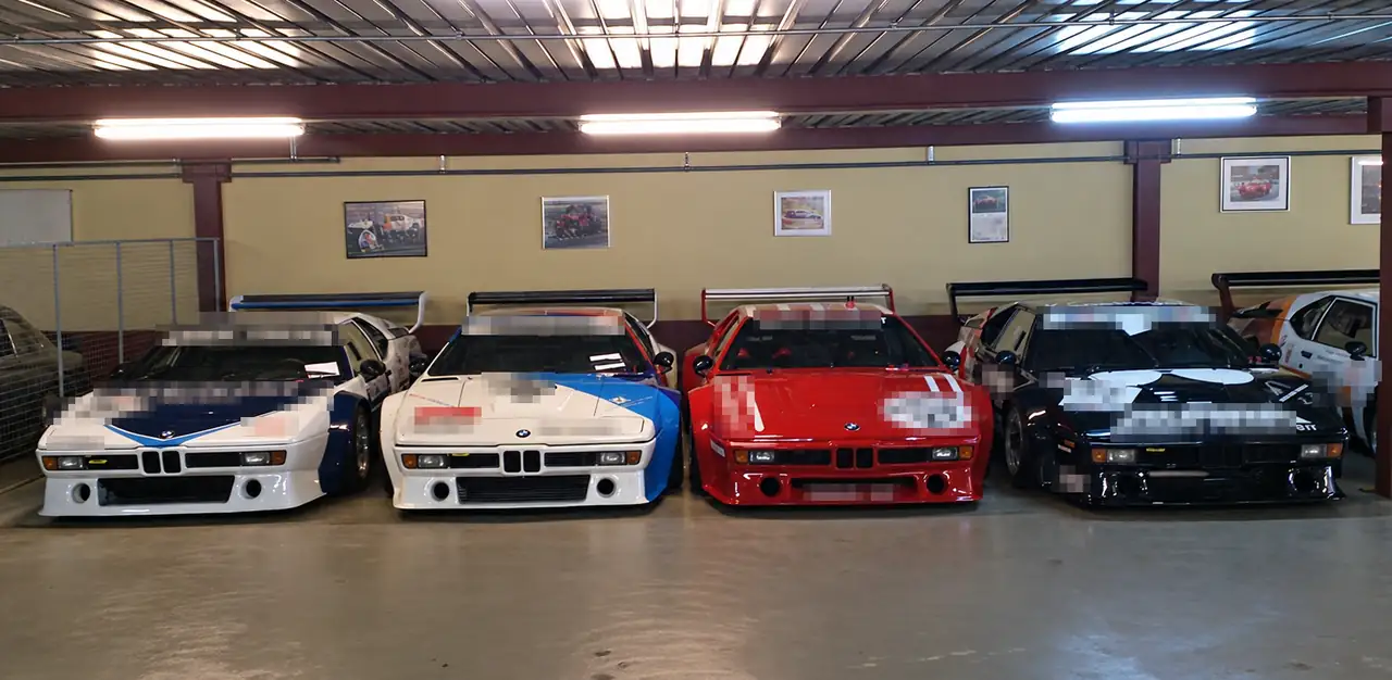 Vier BMW M1 Procar in einer Reihe in der Halle, Sponsorenschriften verpixelt